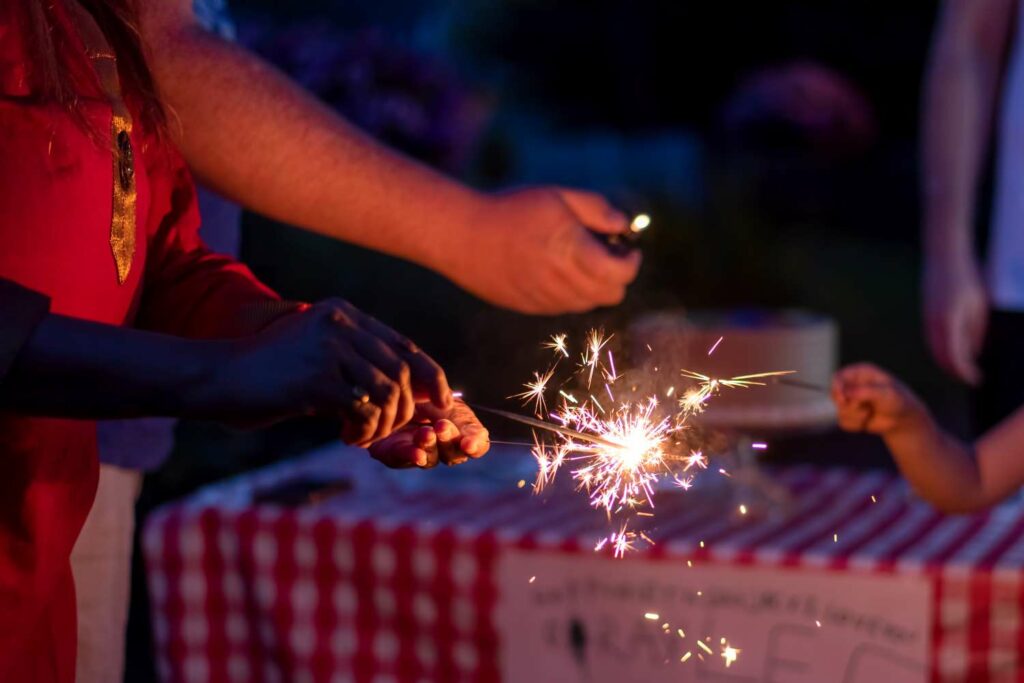 hands holding sparklers in front of picnic table