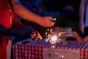 hands holding sparklers in front of picnic table