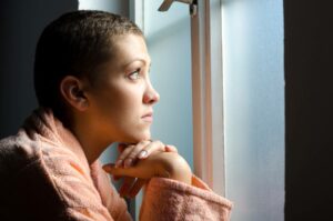 woman with shaved head looking out window in a sad way