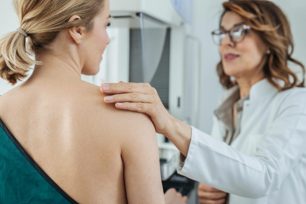 woman in hospital gown receiving breast examination from female doctor
