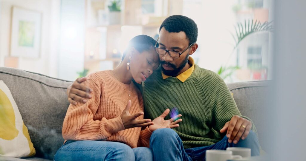 middle age black couple on couch with man holding sad woman