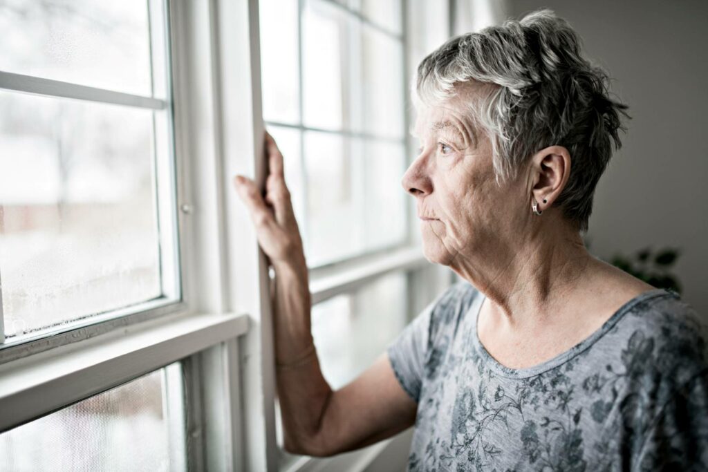 old white woman staring out window in a depressed way
