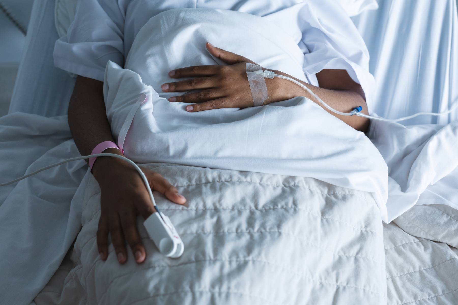 African American woman's hands hooked up to medical devices, laying in bed